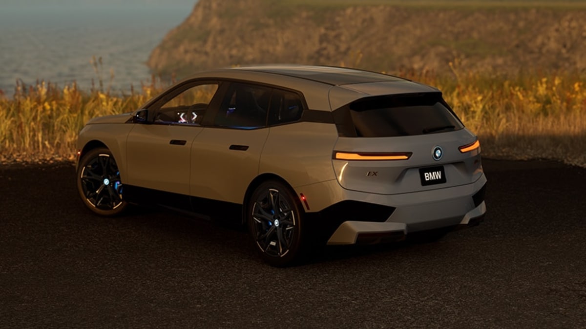 A darker gray BMW iX parked next to a field on a hill. A darker gray BMW iX parked next to a field on a hill.