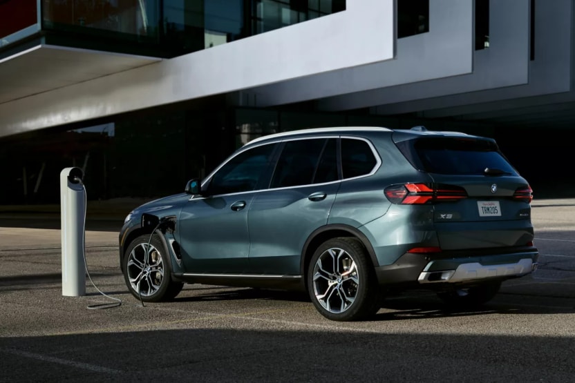 A greenish-blue BMW X5 plugged into a charging station in a parking lot.