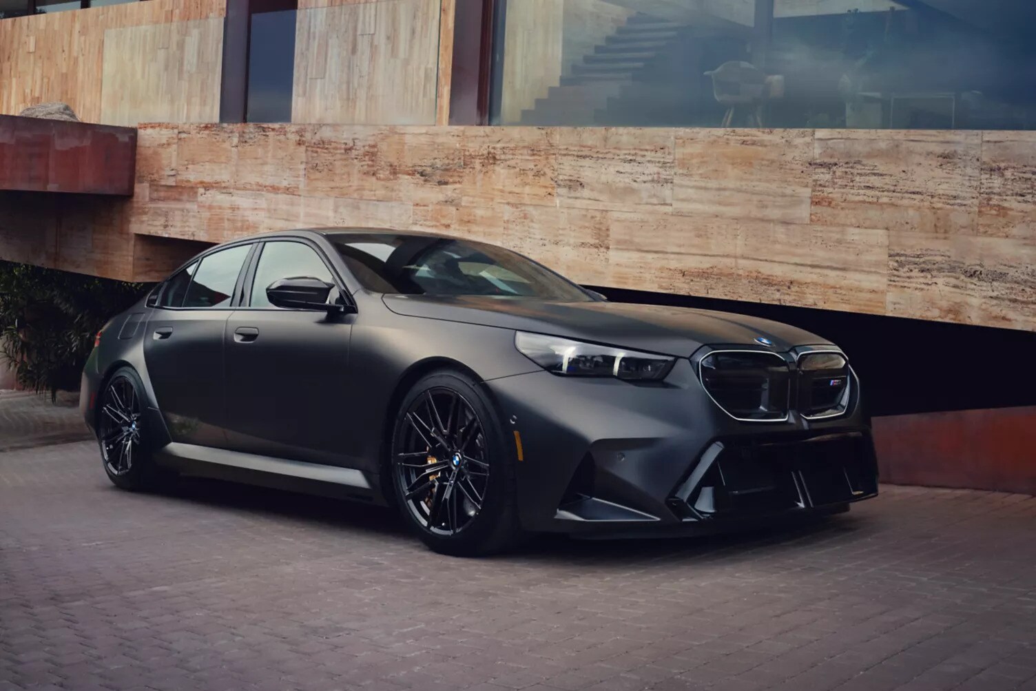 A black BMW M5 parked next to a luxury home. A black BMW M5 parked next to a luxury home.