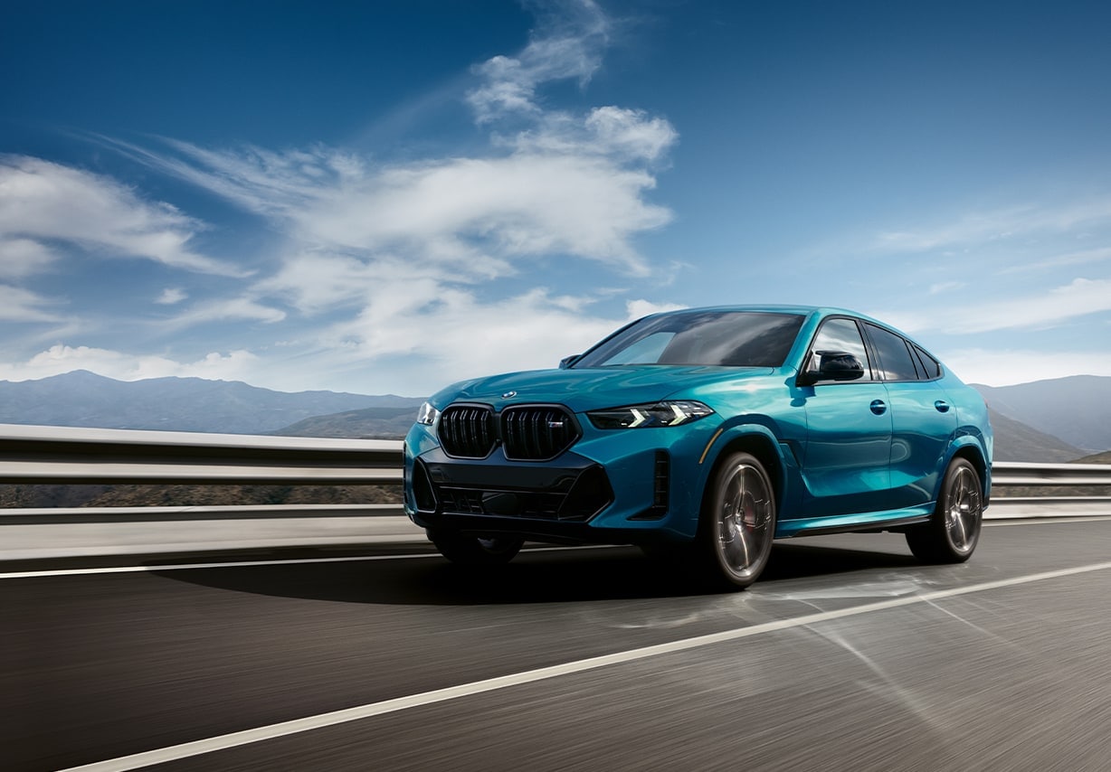 A turquoise BMW X6 driving down the road.