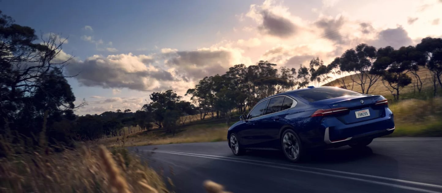A blue BMW 5 Series driving along the road near some trees and plains. A blue BMW 5 Series driving along the road near some trees and plains.