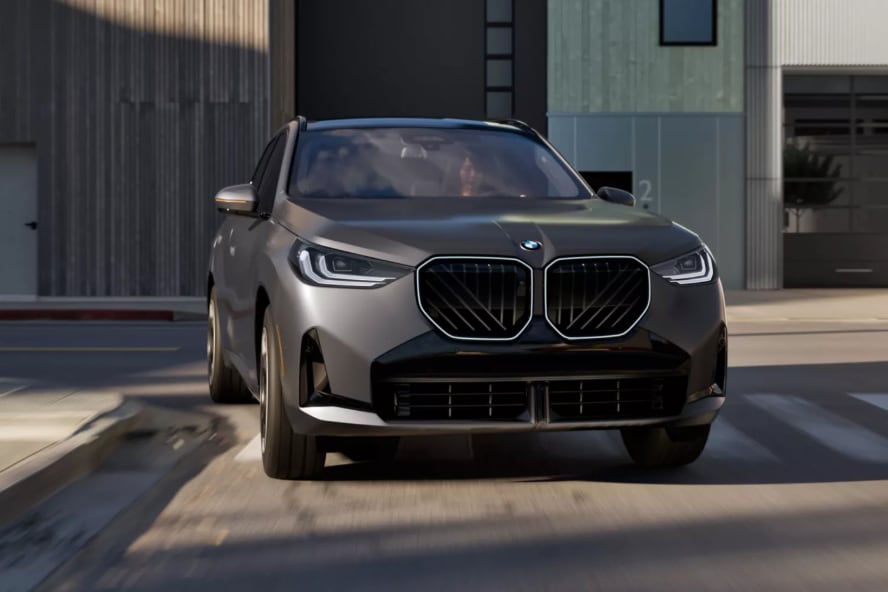 A gray BMW X3 driving over a crosswalk in a city.