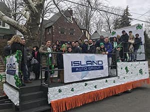 Island Auto Group team riding a decorated parade float with shamrock decorations during a St. Patrick's Day parade
