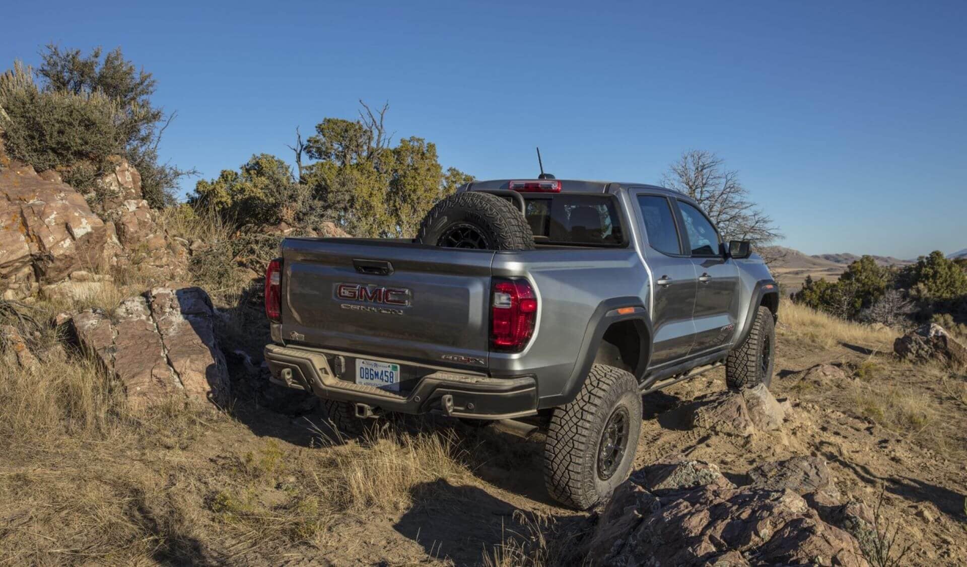 A GMC Canyon AT4 navigating a narrow, rocky trail near Superstition Mountain, its 33” tires gripping volcanic scree after towing a teardrop trailer to a remote campsite.