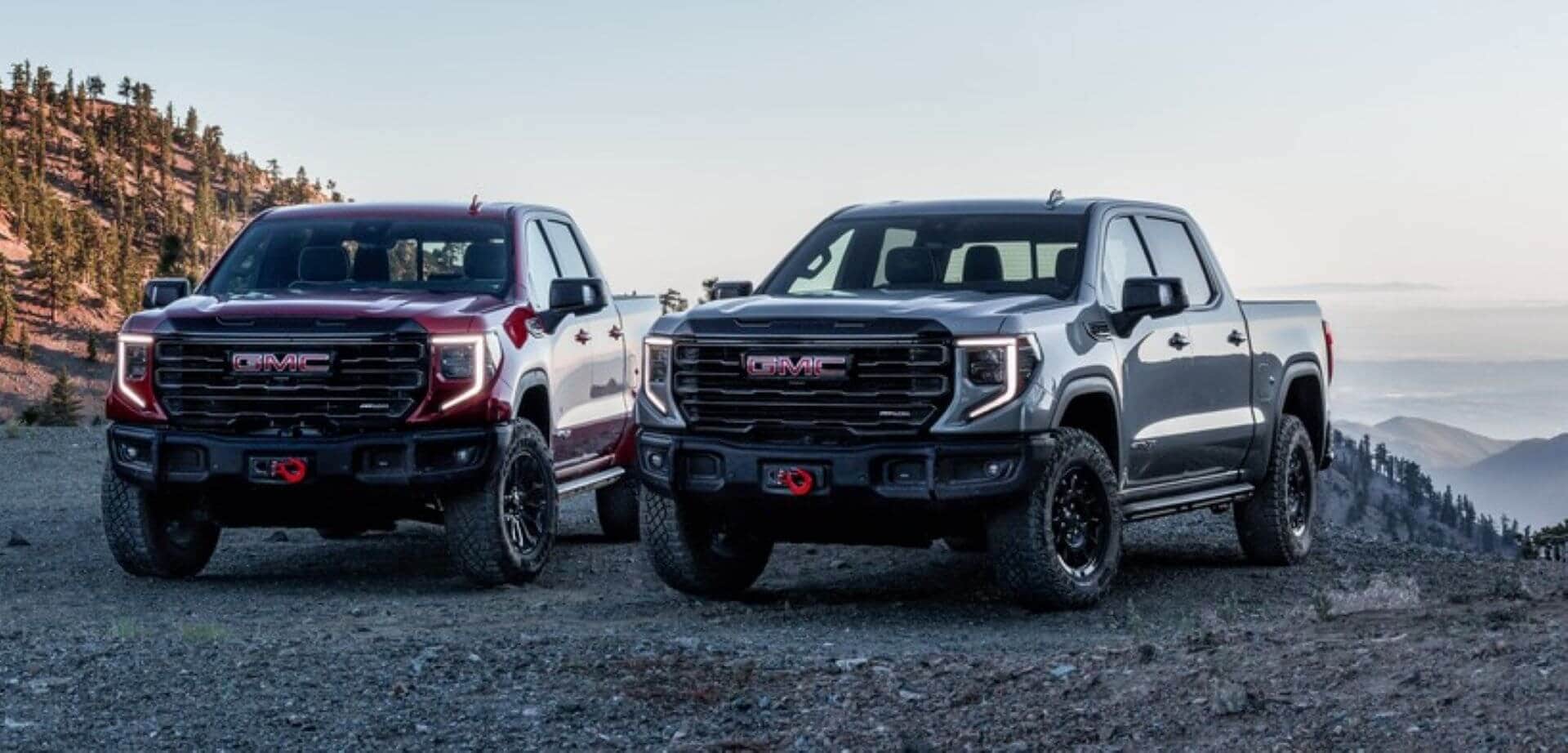 Side-by-side comparison of a GMC Sierra 1500HD AT4 and AT4X towing boats along the Salton Sea shoreline, foggy clouds swirling behind them.