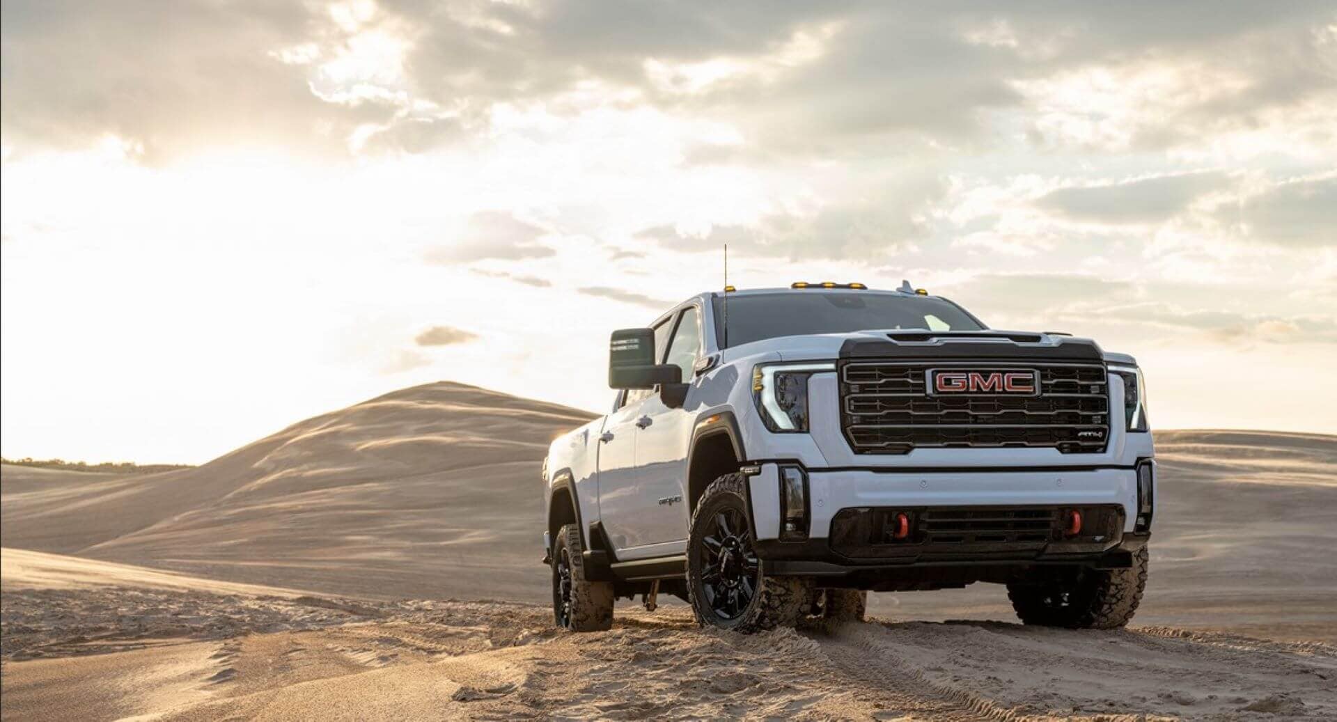 A GMC Sierra 2500HD AT4 exploring after hauling a fifth-wheel trailer across the sunbaked desert flats near Glamis Sand Dunes, its dual rear wheels kicking up dust as it navigates a steep incline.