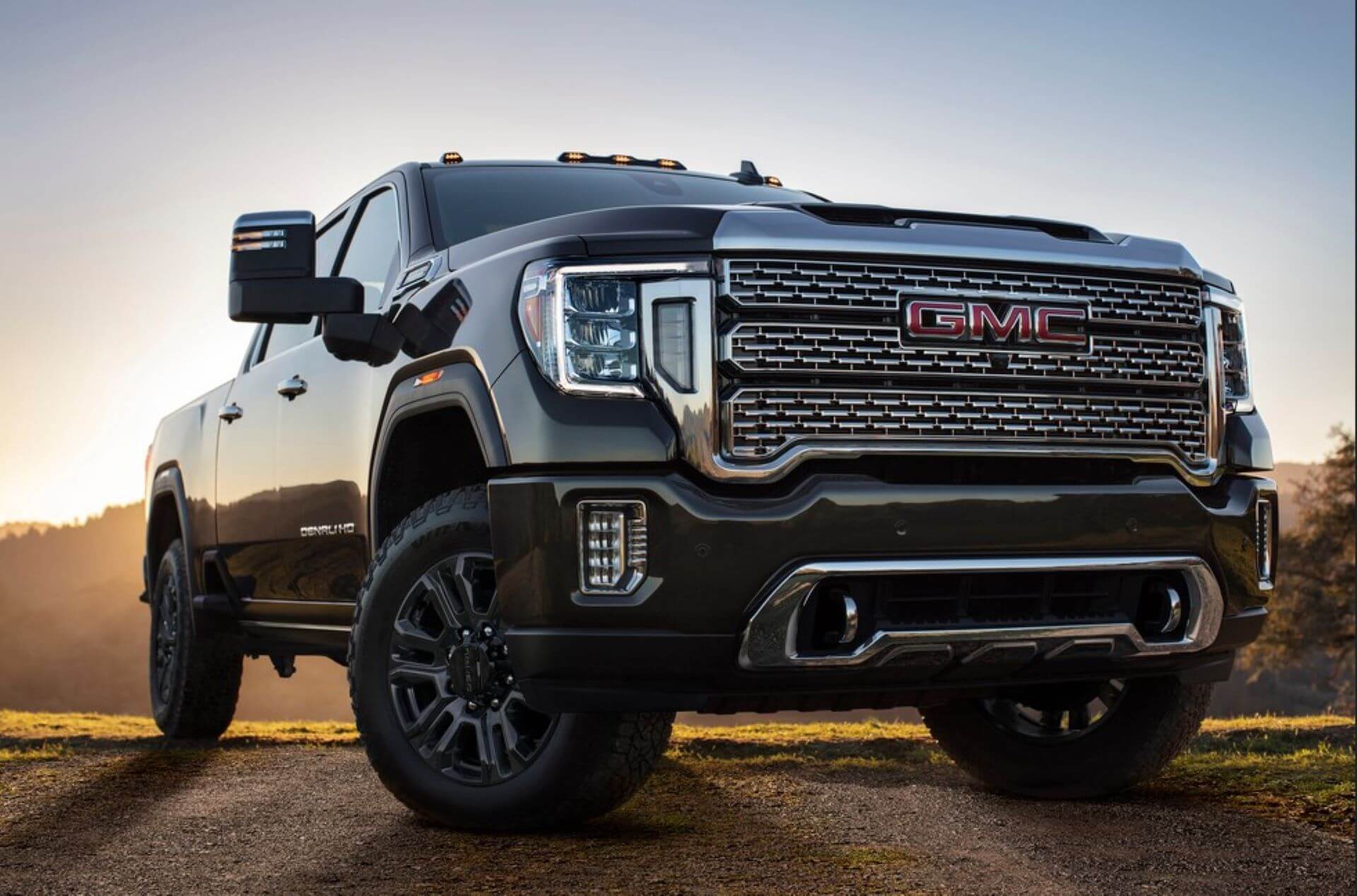 A GMC Sierra 1500 AT4 with a compact camper hitched behind it, parked at a sandy pullout overlooking the Salton Sea, its Integrated Trailer Camera displaying a clear rear view.
