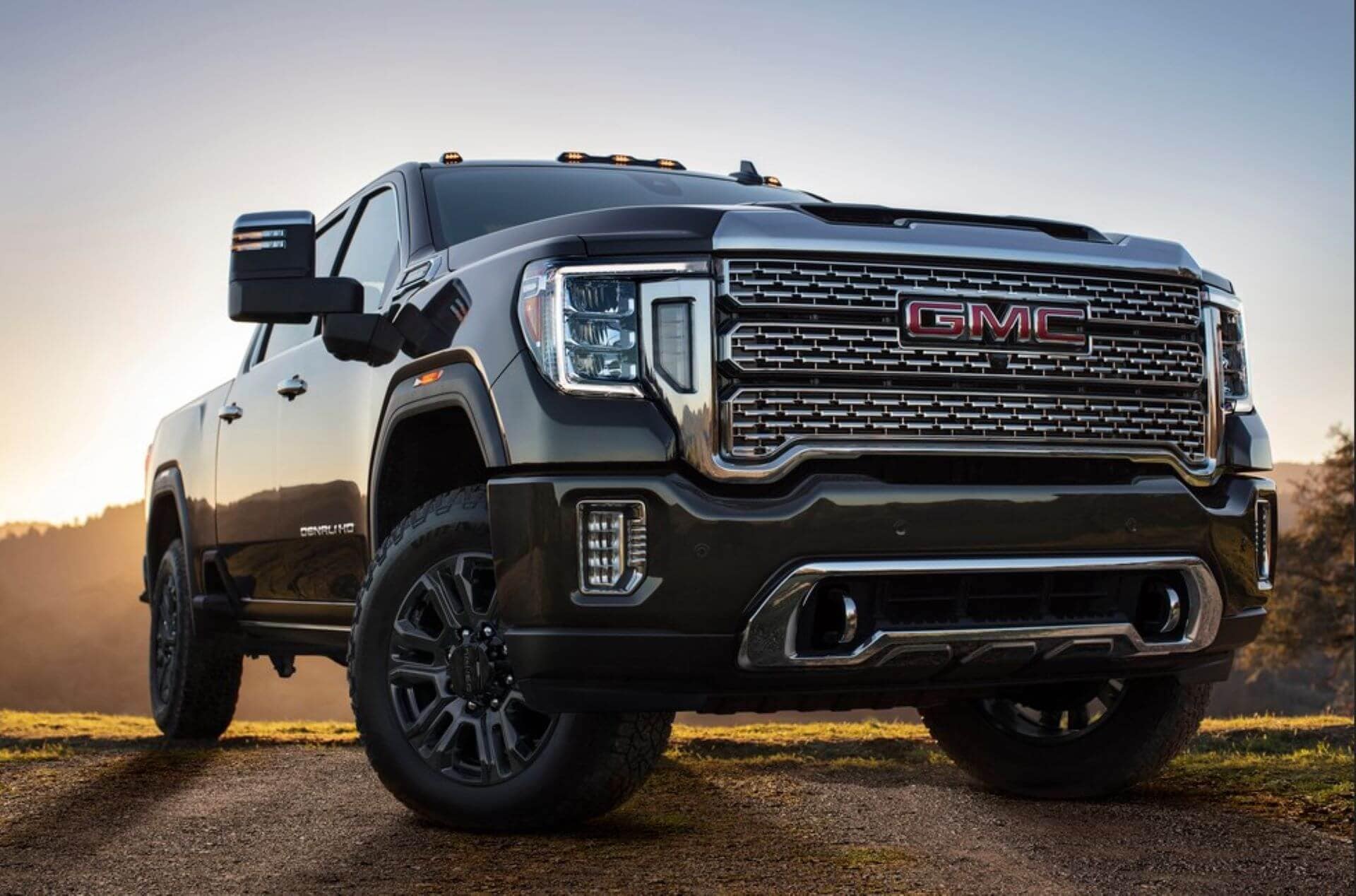 A GMC Sierra 1500 AT4 with a compact camper hitched behind it, parked at a sandy pullout overlooking the Salton Sea, its Integrated Trailer Camera displaying a clear rear view.