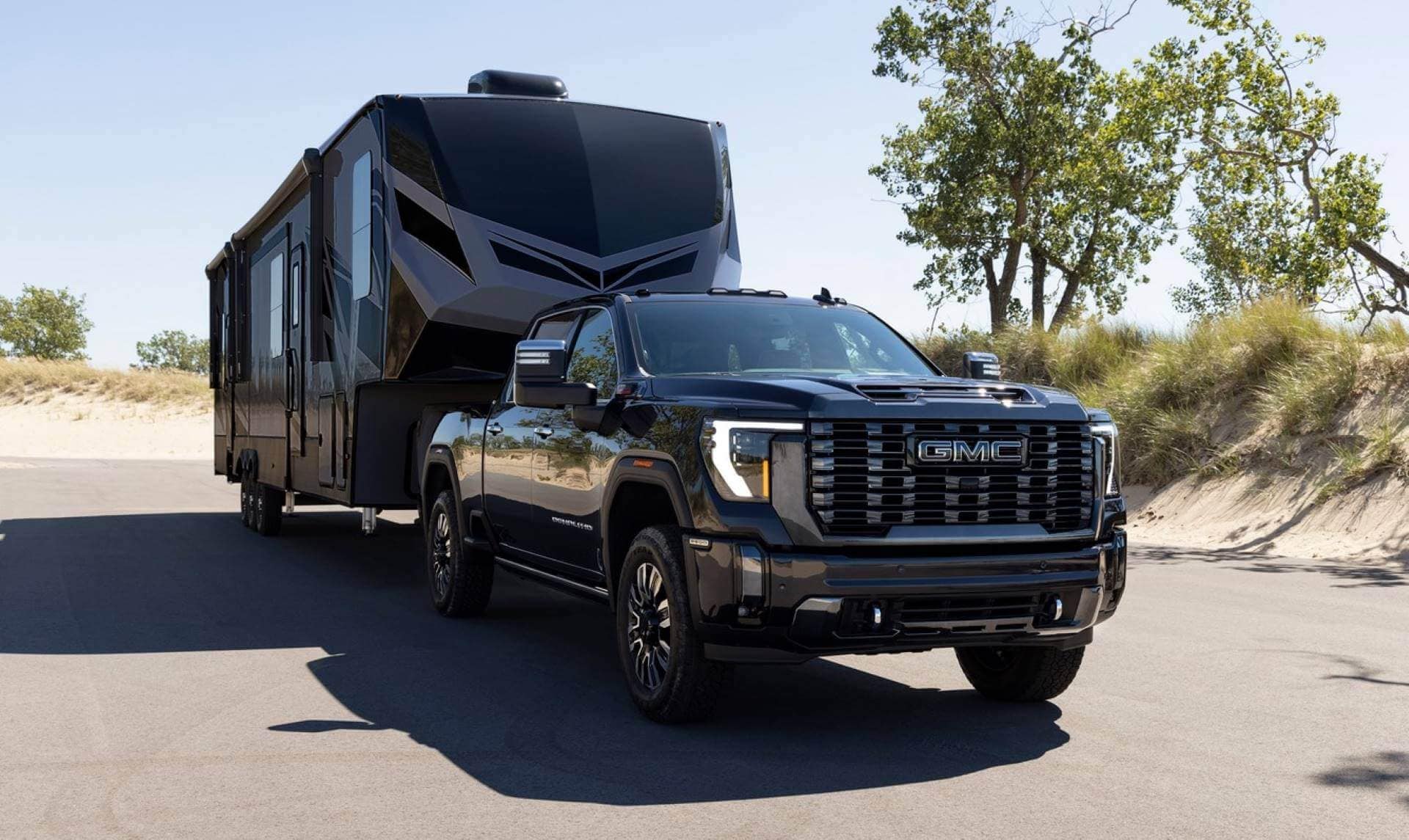 A black GMC pickup towing a large trailer, fifth-wheel