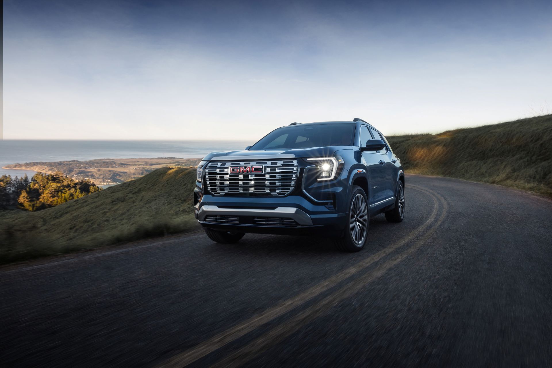 Front 3/4 view of the 2026 GMC Terrain in Downpour Metallic driving on a winding road.