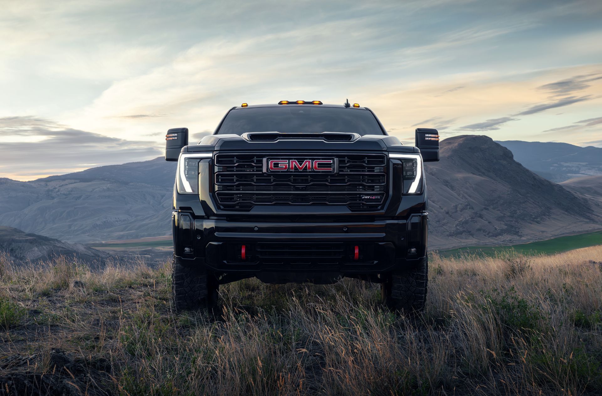 a GMC Sierra 2500HD sitting atop high grassy bluffs with red recovery hooks featuring prominently