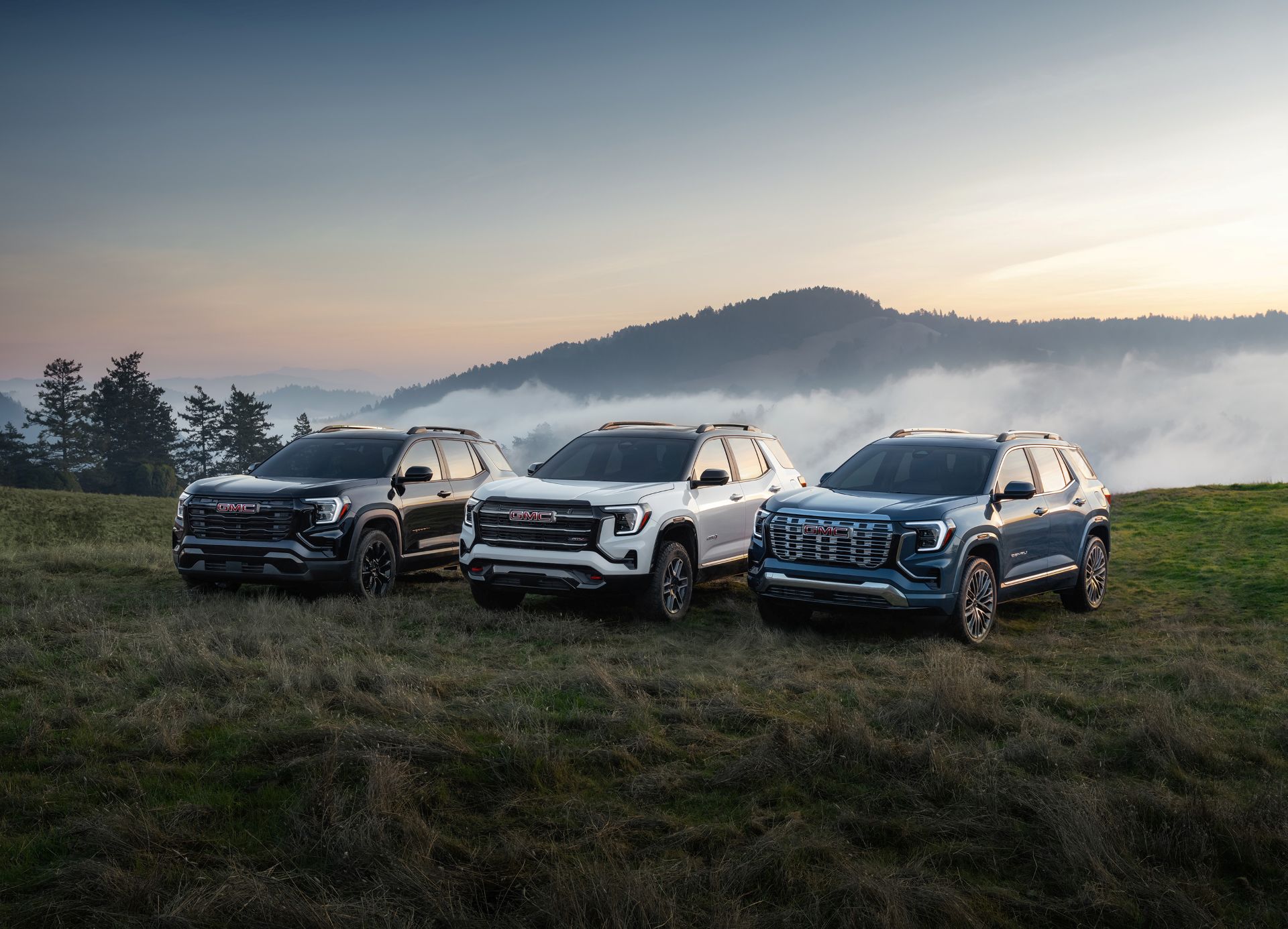 Pack shot of the next generation GMC Terrain lineup, including Elevation in Ebony Twilight Metallic, AT4 in Summit White, and Denali in Downpour Metallic, from left to right.