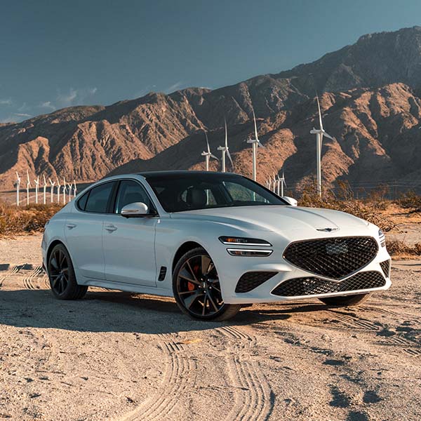 Model Features of the 2022 Genesis G70 at Genesis of York | White 2022 Genesis G70 Driving on Dirt Road with Wind Turbines in Background
