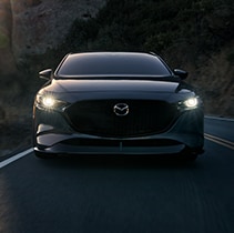 Model Features of the 2021 Mazda3 at Jack Giambalvo Mazda | Close up of Mazda3 driving with headlights on