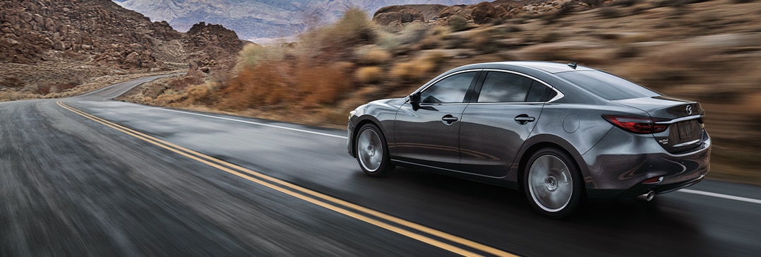 The 2021 Mazda3 vs. The 2021 Mazda6 at Jack Giambalvo Mazda | Mazda6 speeding down road with mountains