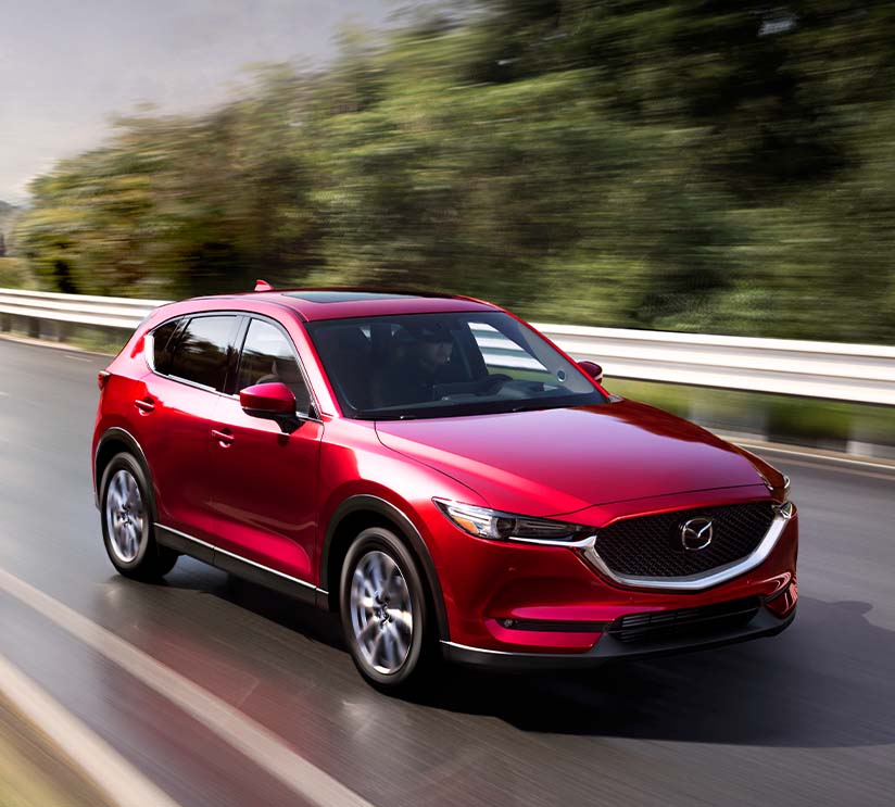 Model Features of the 2021 Mazda CX-5 at Jack Giambalvo Mazda | Red 2021 Mazda CX-5 Driving Fast Past Trees