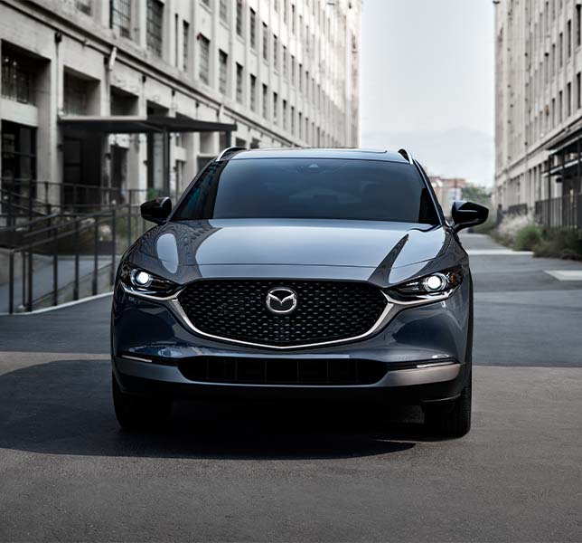 Model Features of the 2021 Mazda CX-30 at Jack Giambalvo Mazda | Blue 2021 Mazda CX-30 Driving In Between Buildings in the City