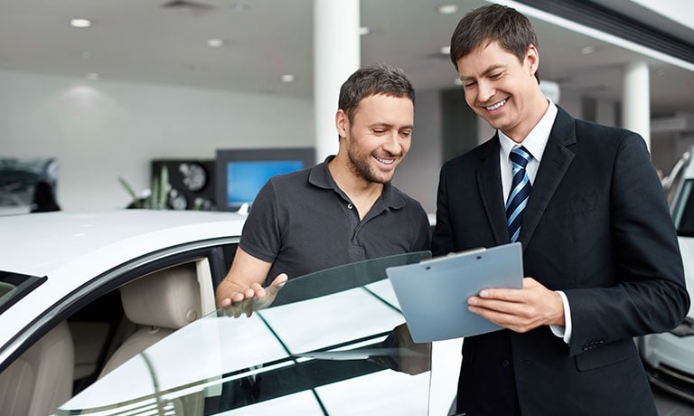 Two men looking at clipboard in front of car