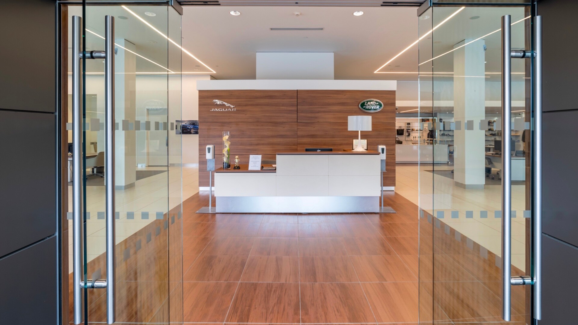 Land Rover White Plains Hours and Directions Close up looking into the doors of Land Rover White Plains. A desk is visible in the center with a Jaguar logo above it on the top left, and a Land Rover logo on the top right..