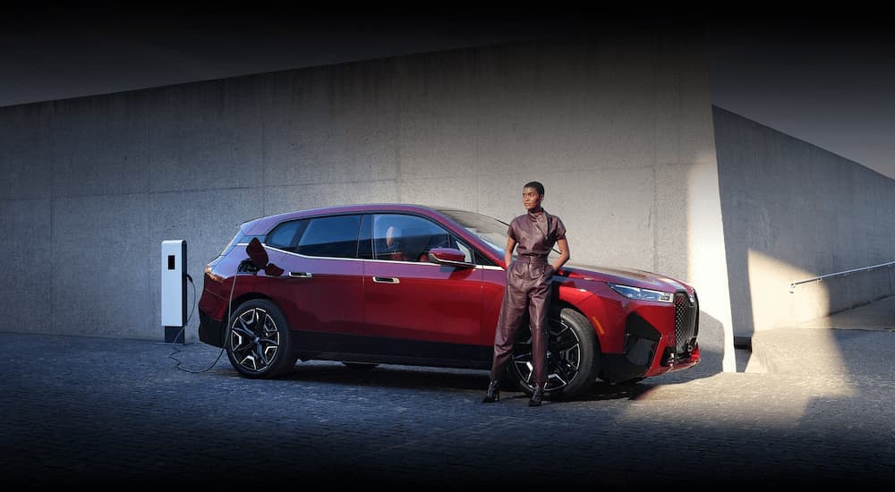 A red 2023 BMW iX is shown parked in front of a building.