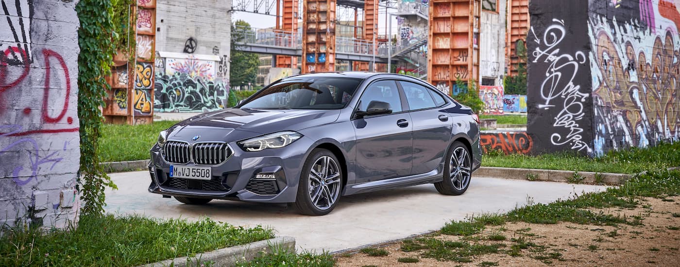 A grey 2021 BMW 2 Series Gran Coupe, a popular BMW, Cincinnati drivers enjoy is parked next to buildings covered in graffiti.