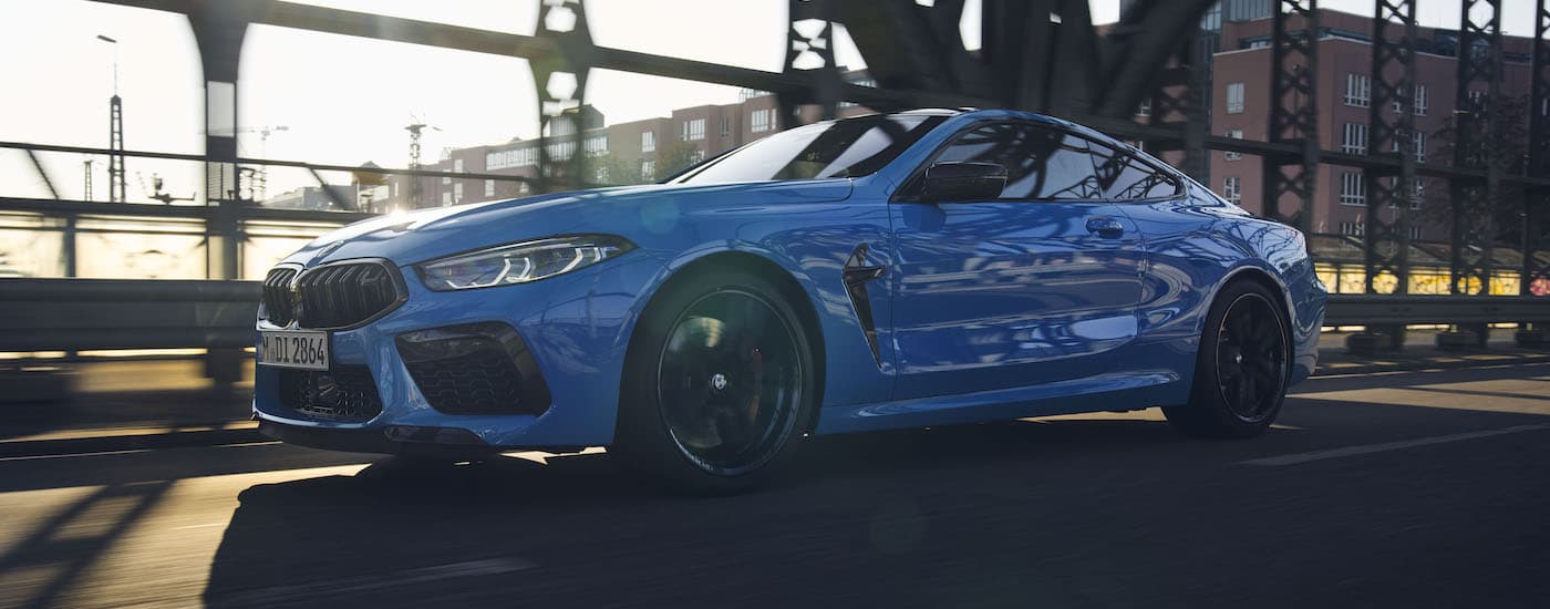 A blue 2022 BMW M8 Competition is shown from the side driving over a bridge.