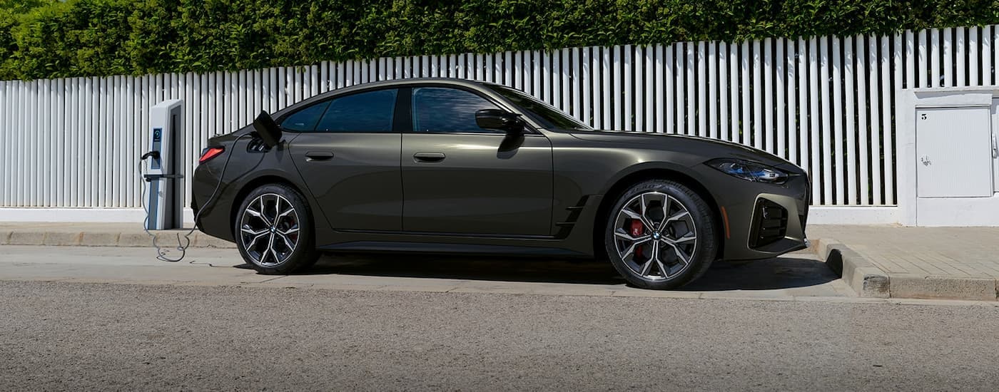 A brown 2023 BMW i4 is shown from the side while charging on a city side street.