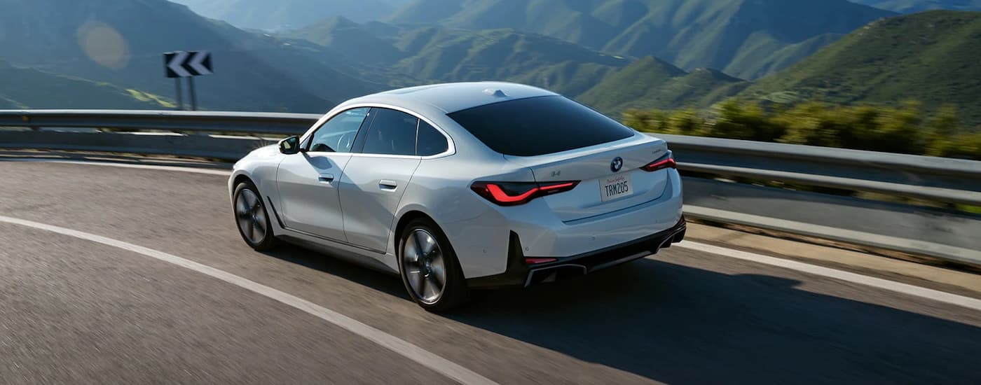 A white 2022 BMW i4 Gran Coupe is shown driving through the mountains after being part of a BMW lease return.