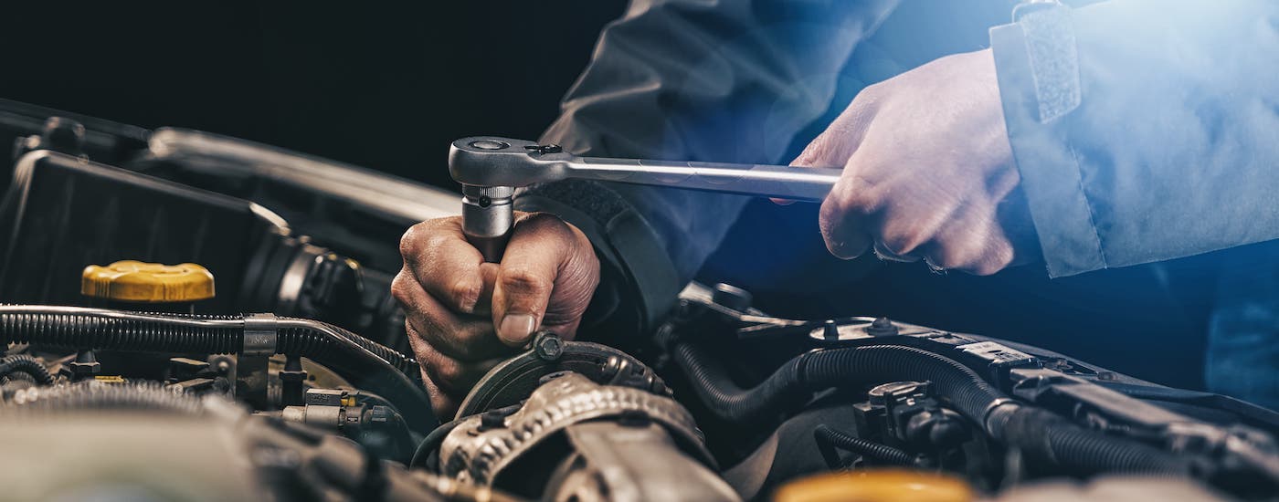 A closeup shows a mechanic using a ratchet on an engine component.