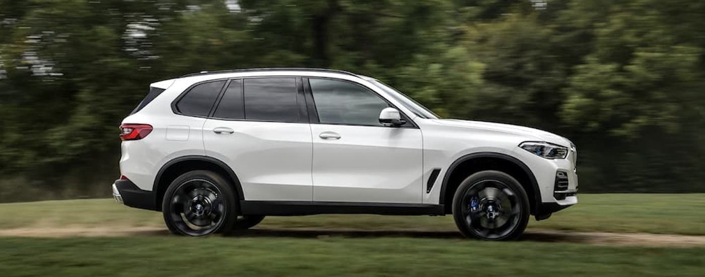 A white 2018 BMW X5 is shown from the side driving past trees.