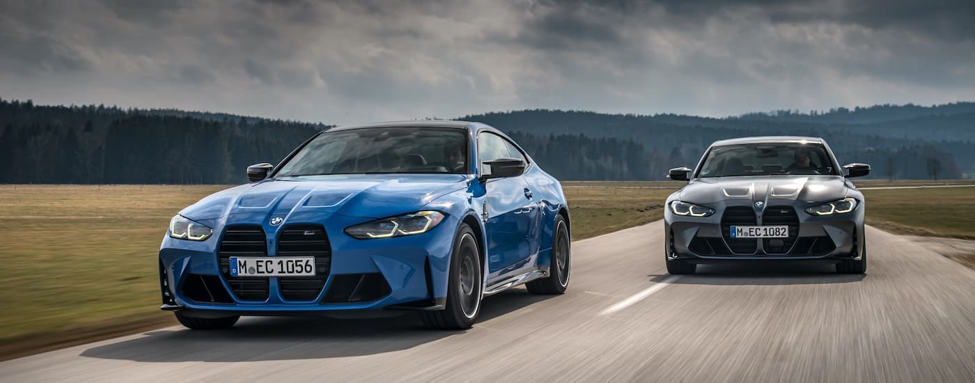 A grey 2021 BMW M3 Competition sedan is shown driving next to a blue 2021 M4 coupe.