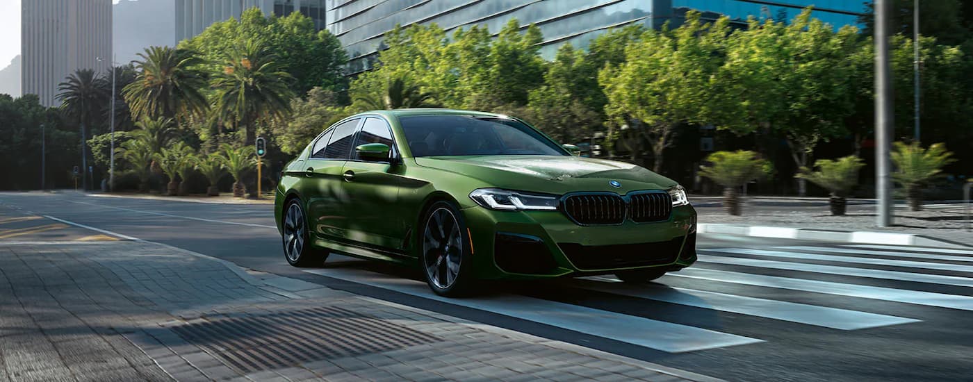 A green 2022 BMW 550i is shown driving on a city street.