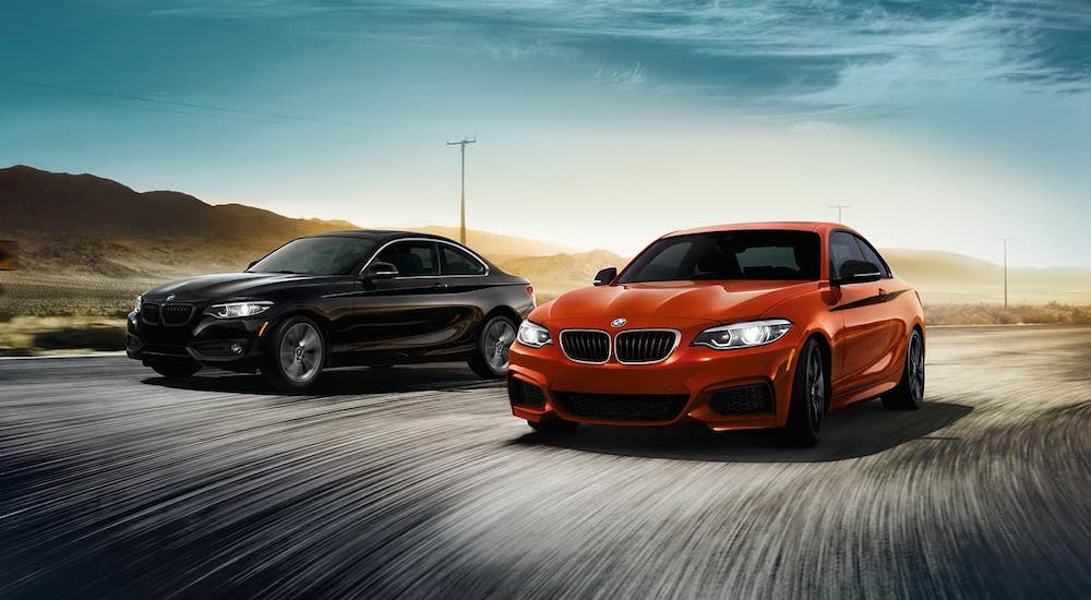 A black and an orange 2020 BMW 2 Series coupes are driving on a track.
