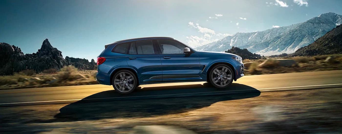A blue 2021 BMW X3 is shown from the side driving on a mountain highway.