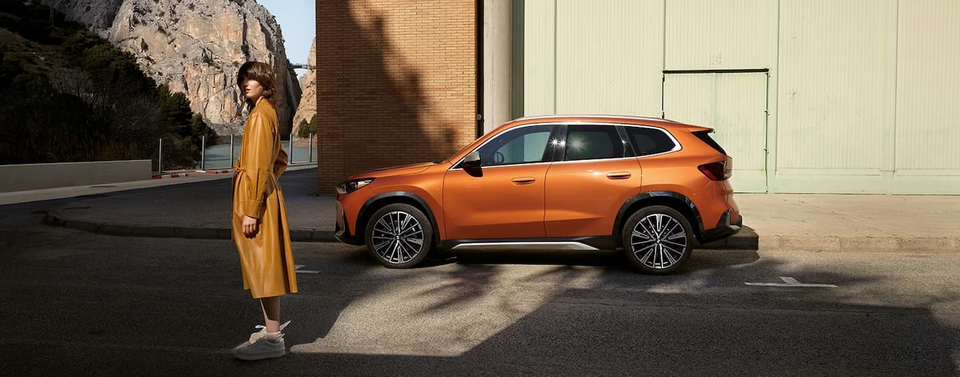 An orange 2023 BMW X1 is shown from the side parked next to a tall building.