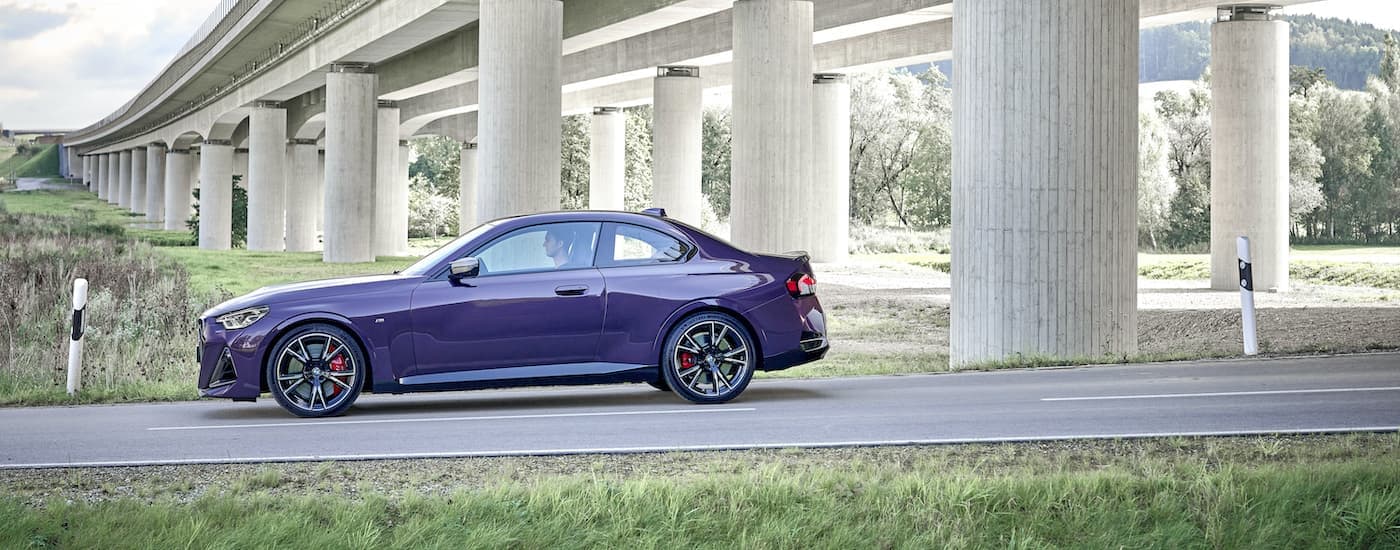 A purple 2021 BMW M240i is shown from the side parked driving under a bridge.