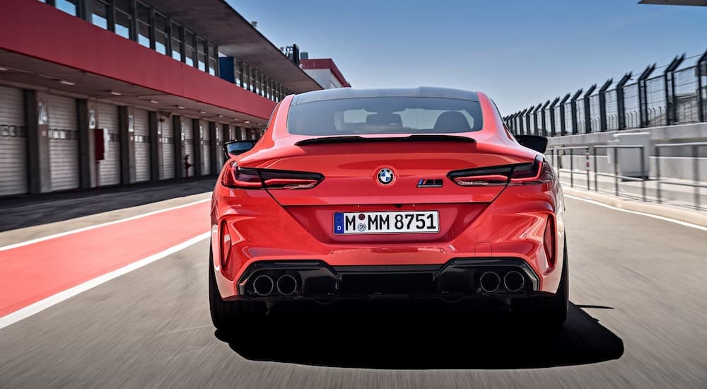 A red 2021 BMW M8 Competition coupe is shown from the rear driving down a race track paddock.