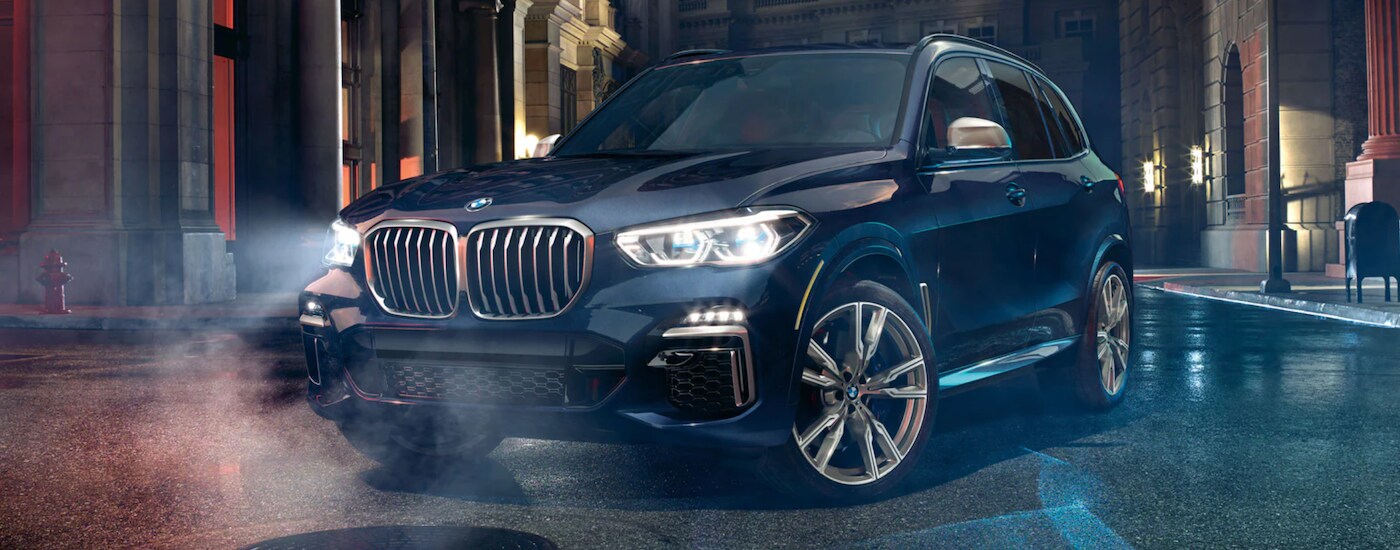 A black 2021 BMW X5 is shown parked in a city with the headlights on at night.