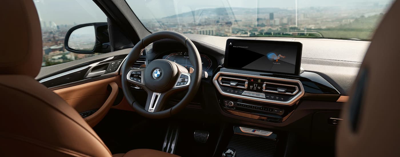 The black and brown interior of a 2023 BMW X3 for sale shows the steering wheel and dashboard.