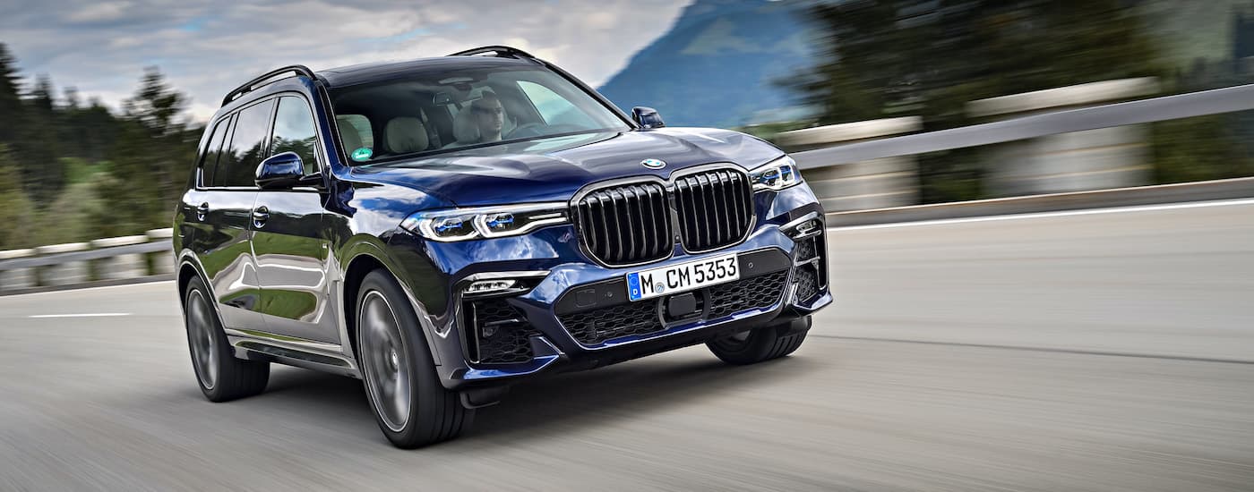A blue 2021 BMW X7 M50i is shown driving past a blurred background.