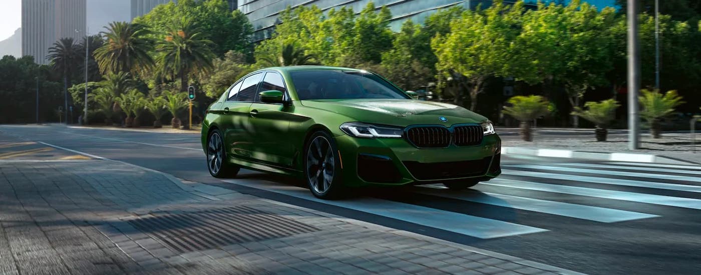 A green 2021 BMW 5 Series is driving on a city street after leaving a BMW dealership near you.