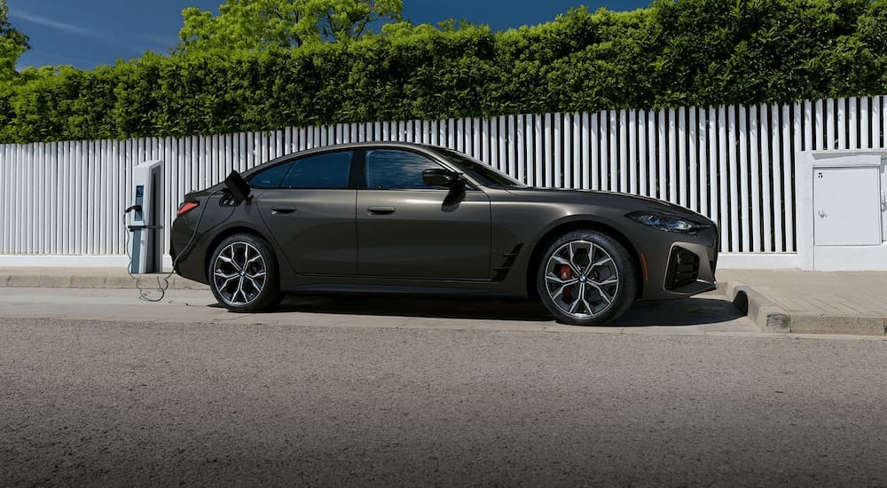 A grey 2023 BMW i4 is shown from the side parked at a charging station.