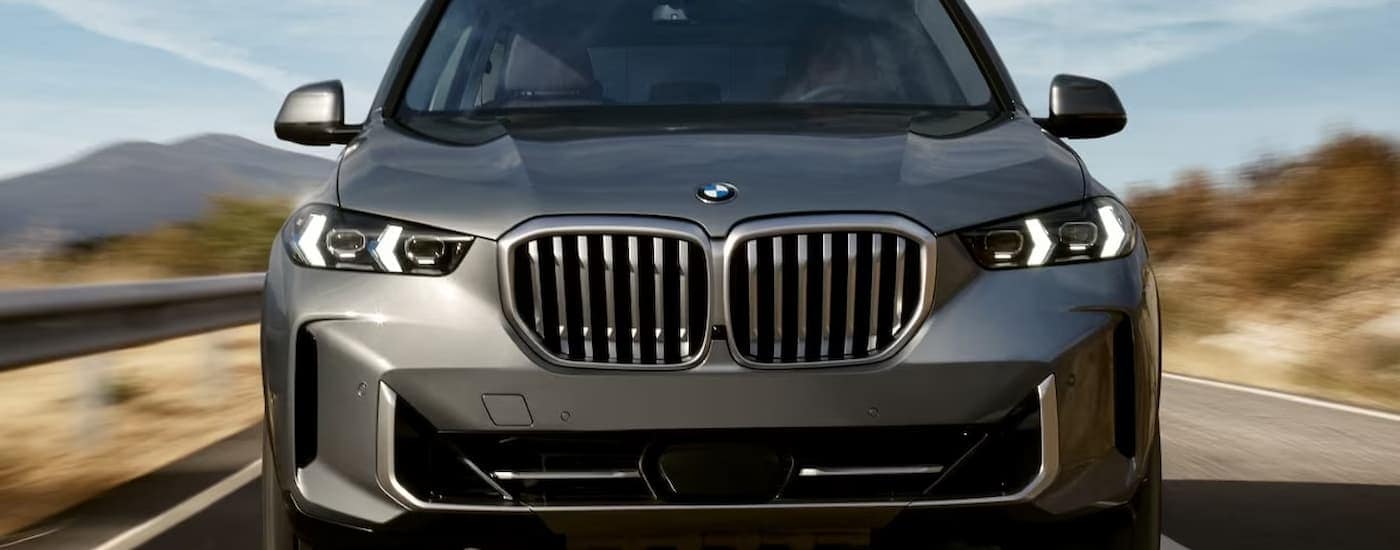 A grey 20232 BMW X5 is shown from the front driving on an open highway.