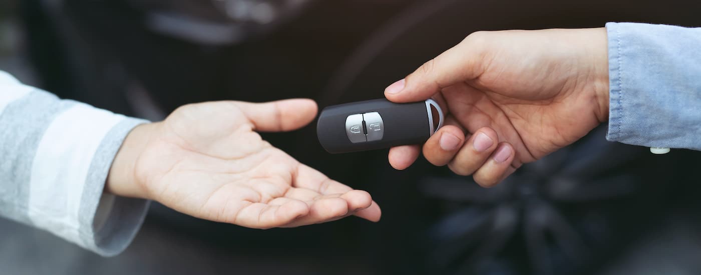 A closeup shows a pair of hands exchanging a car key.