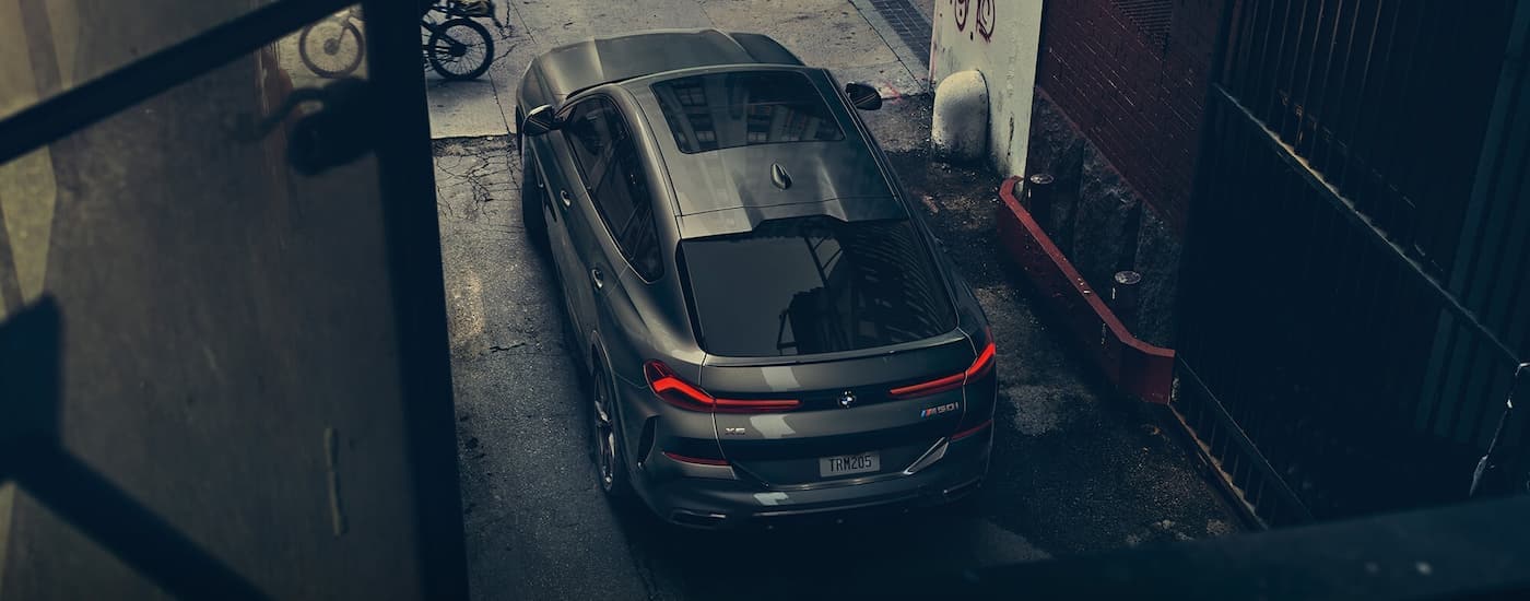 A tan 2022 BMW X6 M501 is shown parked in an alleyway from a high angle.