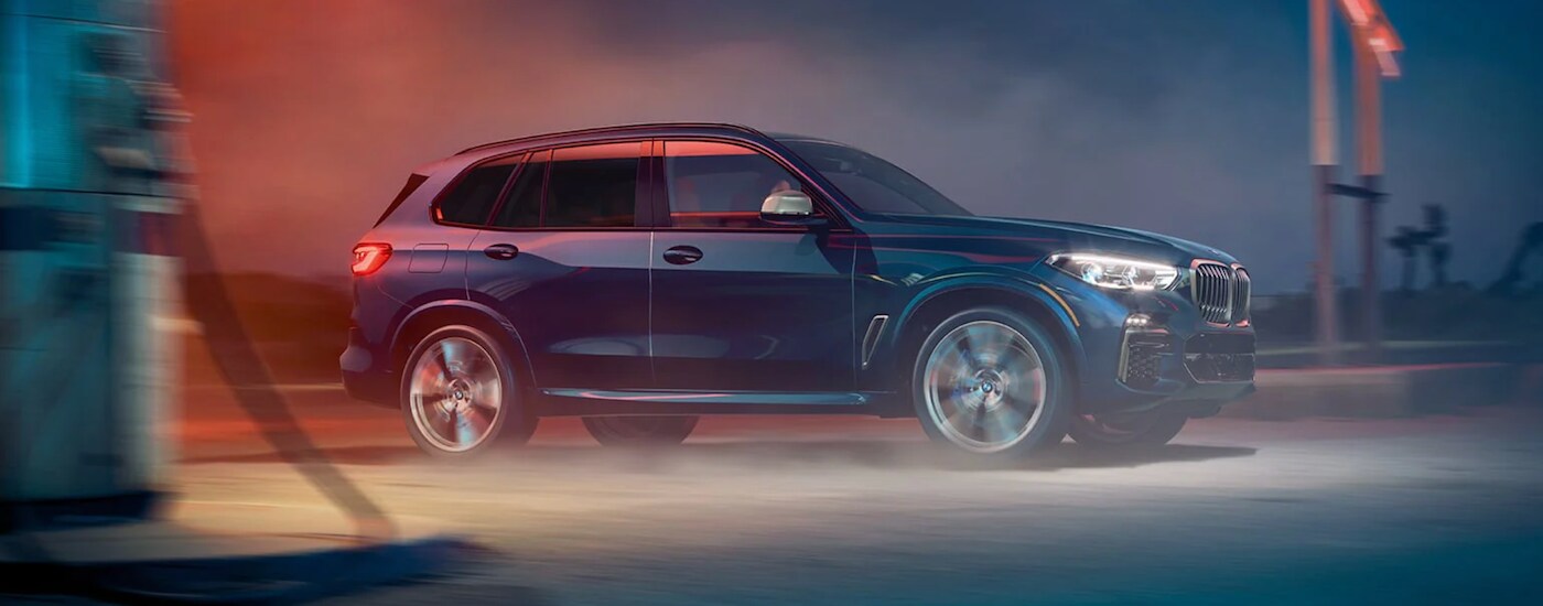 A blue 2021 BMW X5 is shown from the side parked in an alleyway.