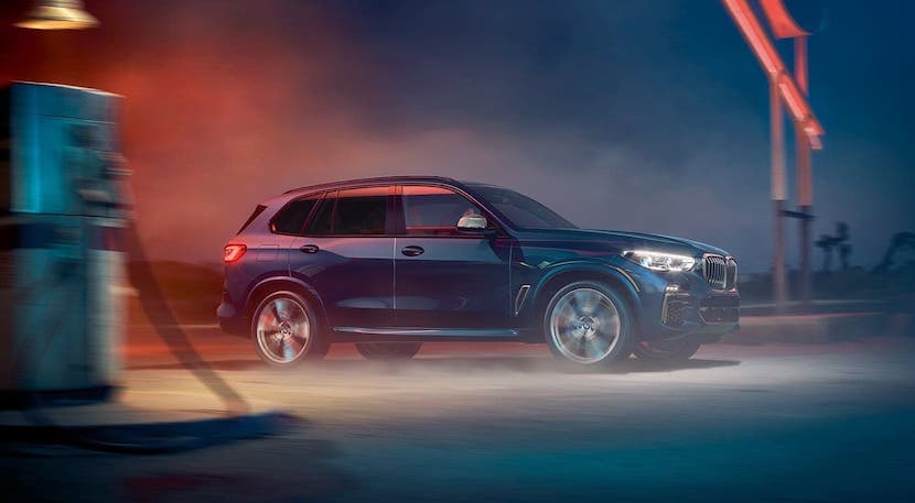 A black 2020 BMW X5 is driving past a gas station at night.