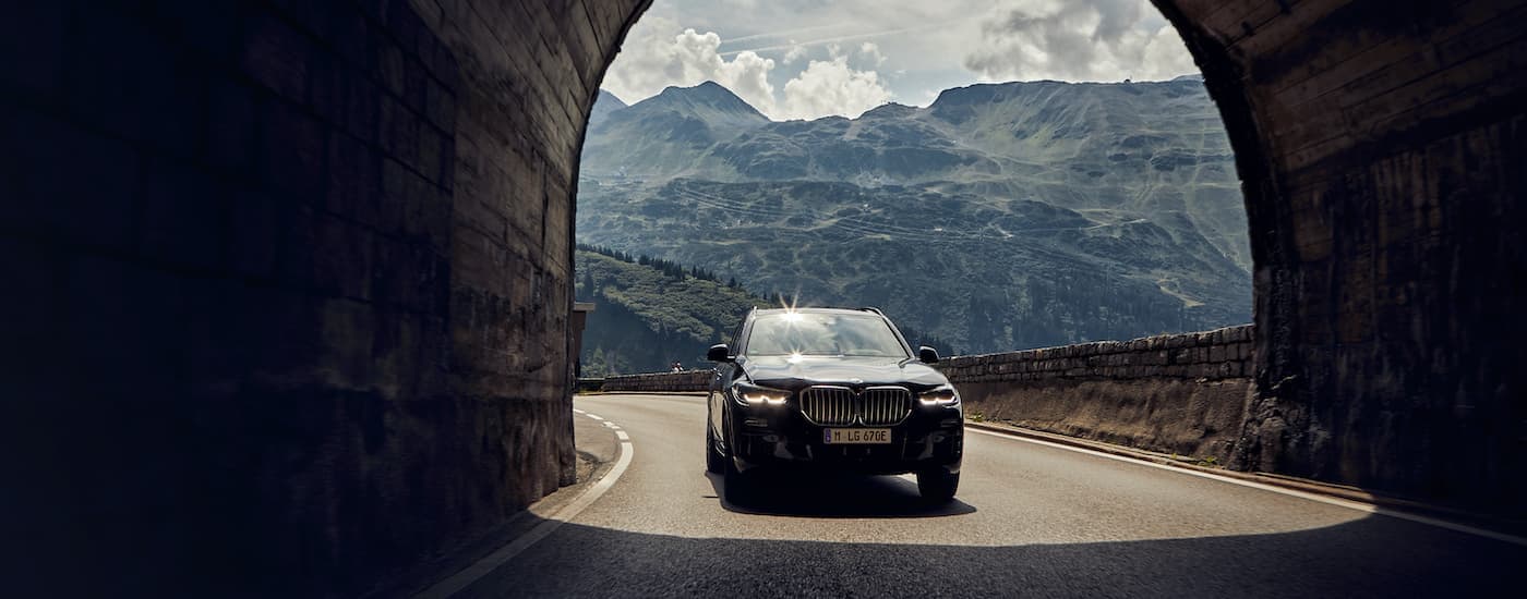 A black 2021 BMW X5 is shown driving through a tunnel in the mountains.