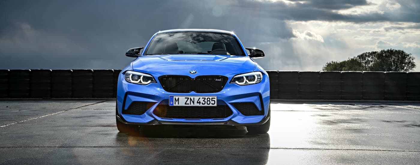A blue 2019 BMW M2 CS is shown from the front parked on wet pavement on a cloudy day.