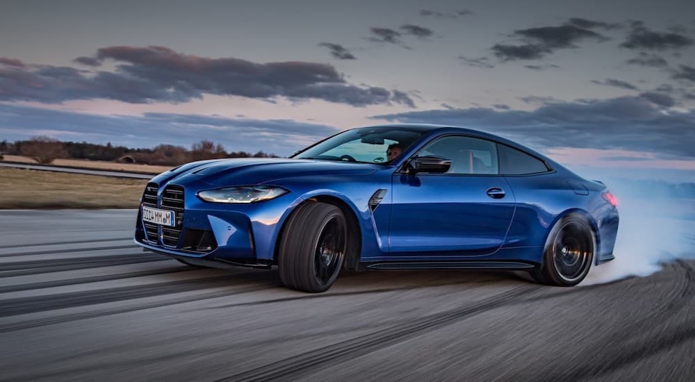 A popular BMW M series vehicle, a blue 2021 BMW M4 Competition coupe is shown from the side spinning its tires.